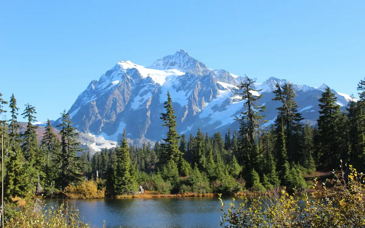 A snow covered peak of the North Cascades above evergreens and a small lake